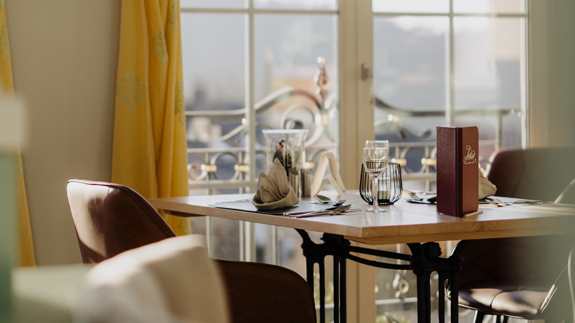 Your restaurant in Rattenberg, Bavaria Dining table with glasses, cutlery, and menu by window with yellow curtains