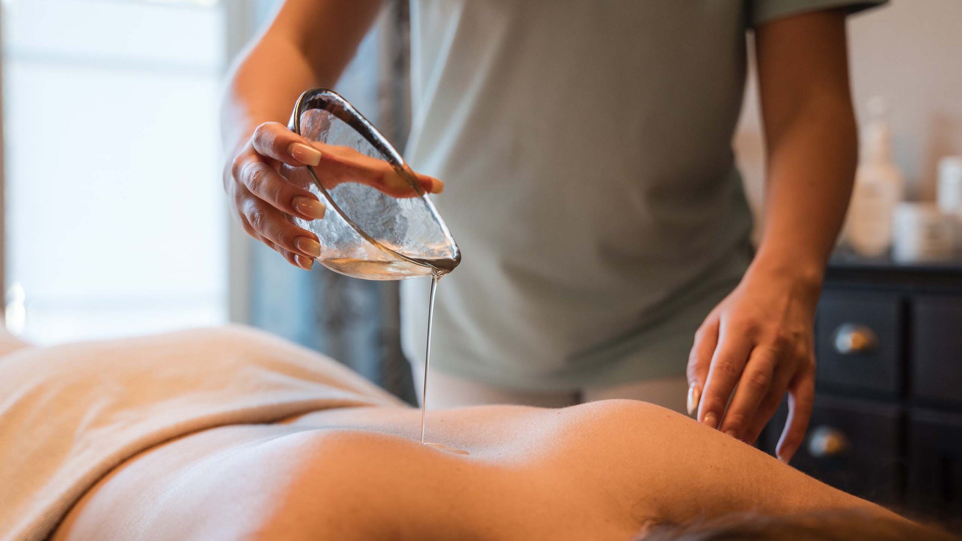 Kosmetik und Massage im Bayerischen Wald Massageöl wird auf den Rücken einer liegenden Person gegossen