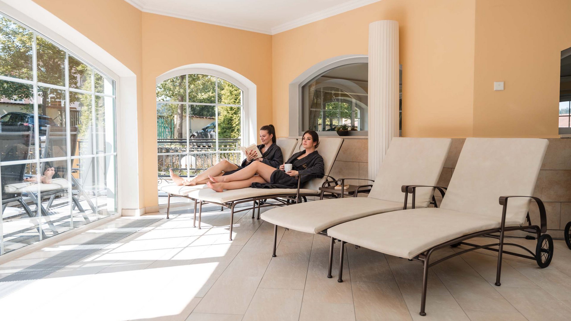A perfect wellness holiday in the Bavarian Forest Two women in robes relaxing on loungers near large windows